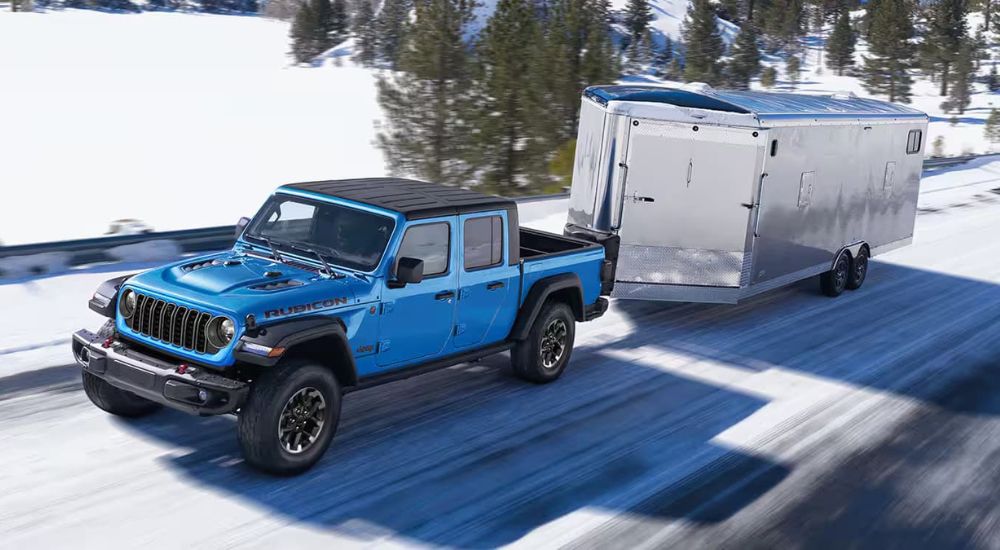 A blue 2024 Jeep Gladiator Rubicon towing a trailer down a snowy bridge.