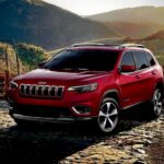 A red 2019 Jeep Cherokee parked off-road after visiting a dealer with used Jeeps for sale.