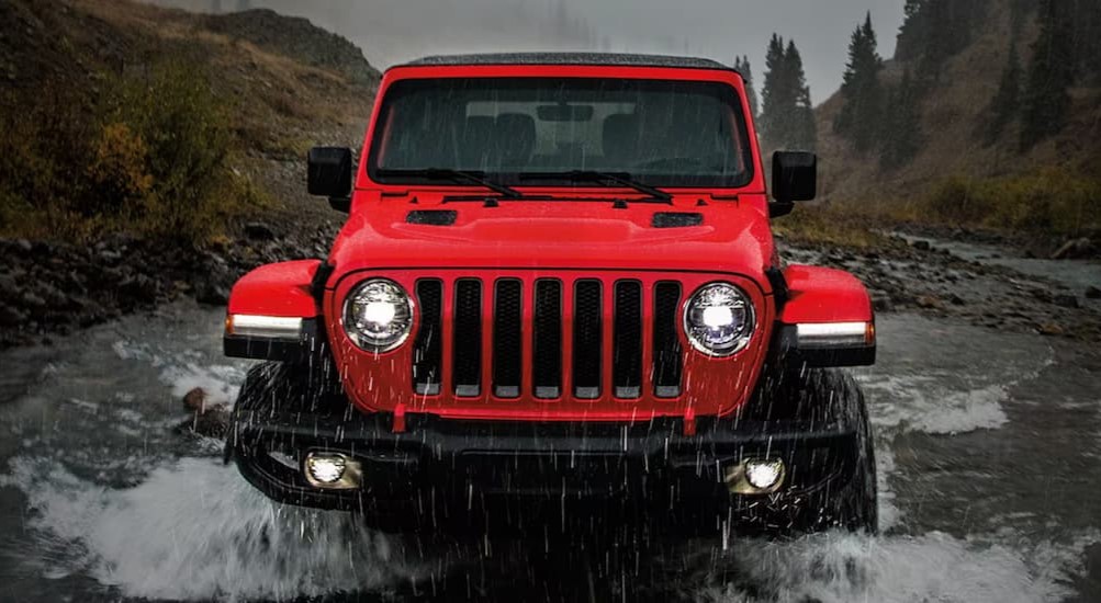 A red 2022 Jeep Wrangler off-roading on a rainy day.