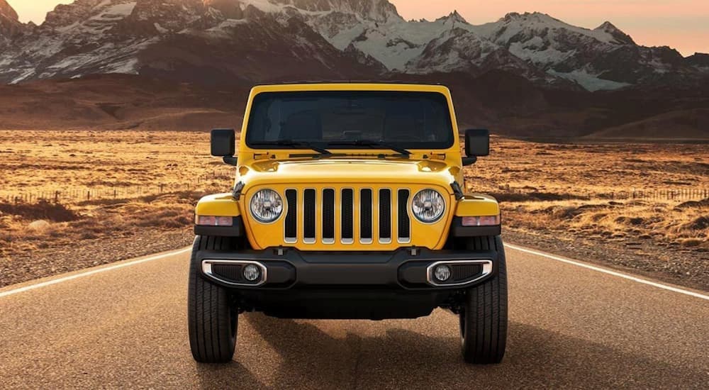 A yellow 2021 Jeep Wrangler driving near mountains.