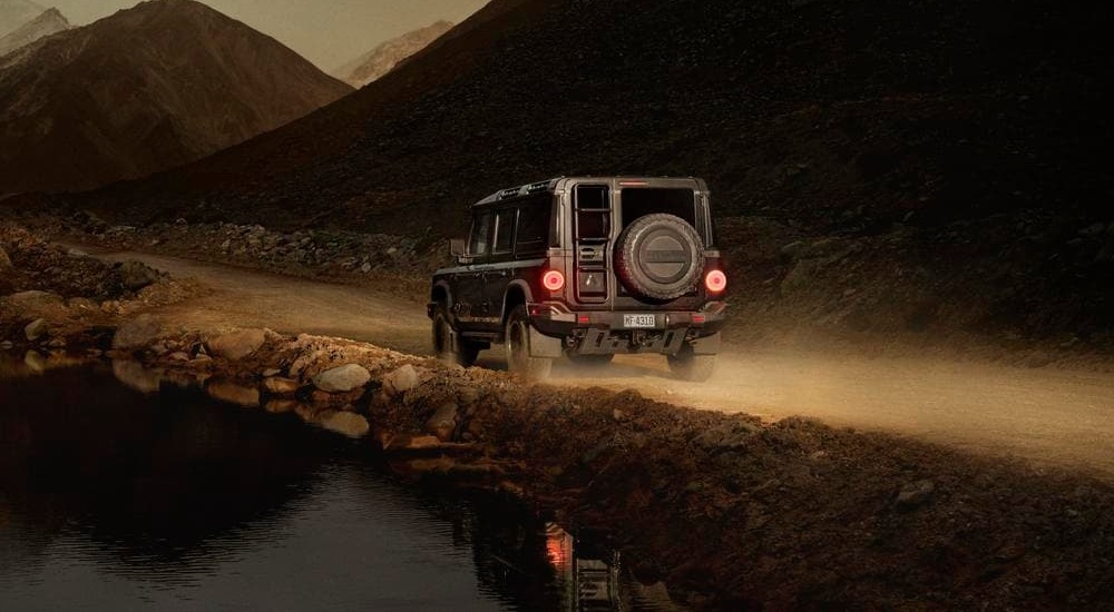Rear of a black 2025 INEOS Grenadier driving off-road by a pond.