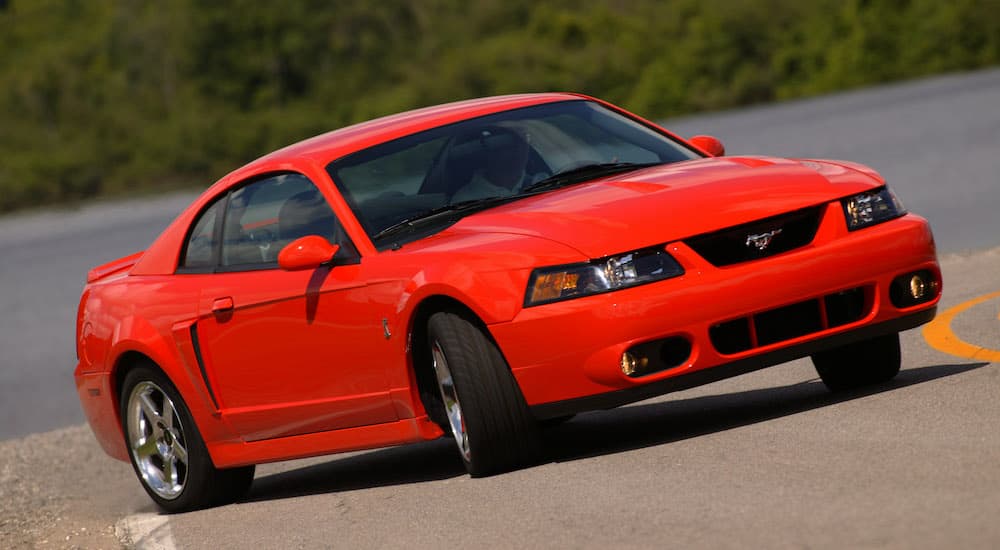 A red 2004 Ford Mustang driving during the day.