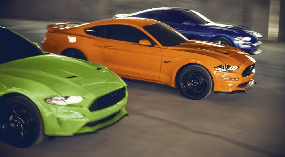 A green, orange and blue 2020 Ford Mustangs racing side-by-side.