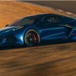 Blue 2027 Chevy Corvette Grand Sport driving through a sand-covered corner.