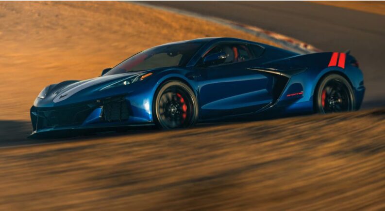 Blue 2027 Chevy Corvette Grand Sport driving through a sand-covered corner.