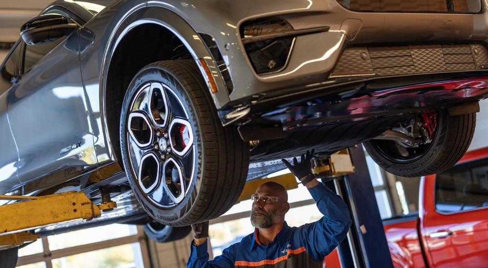 A 2024 Ford Mustang Mach-E on a lift being worked on by a mechanic.