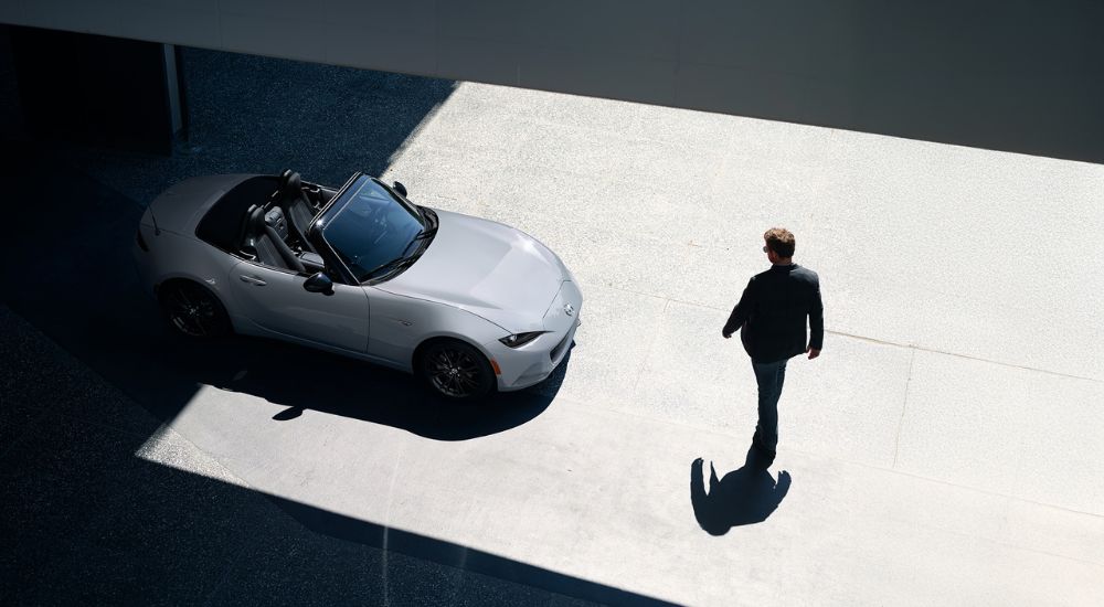A person walking towards their silver 2026 Mazda MX-5 Miata with top down.