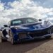 A blue 2025 Chevy Corvette ZR1 is shown driving on a cloudy day.