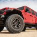 Red 2025 Jeep Wrangler for sale with off-road tires is parked on sandy terrain